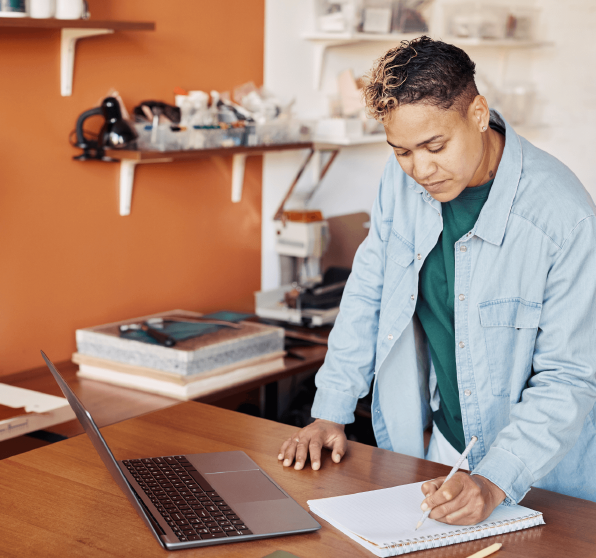 Femme entrepreneure dans son magasin, écrivant sur une feuille, ordinateur devant elle