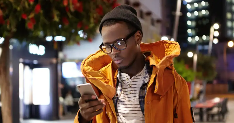 Young black enterpreneur looking at his phone, wearing an orange jacket
