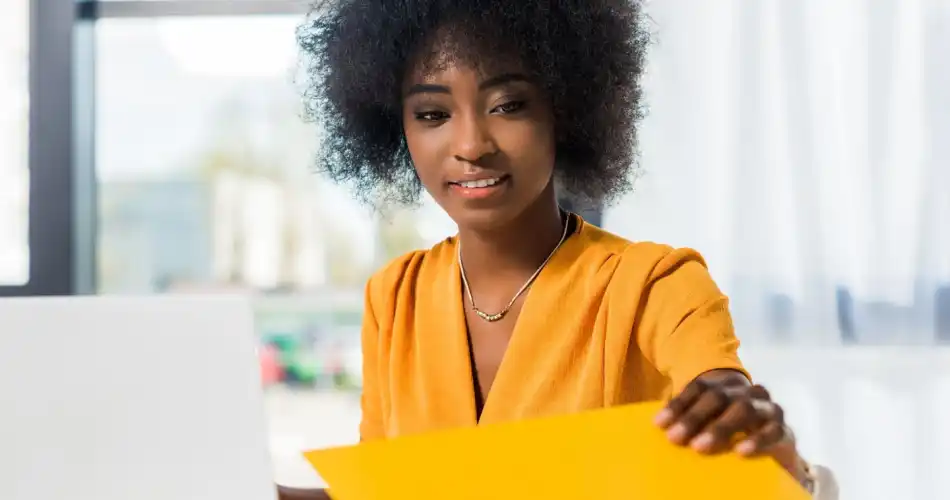 Jeune comptable racisée ouvrant un dossier à son bureau, portant une chemise orange