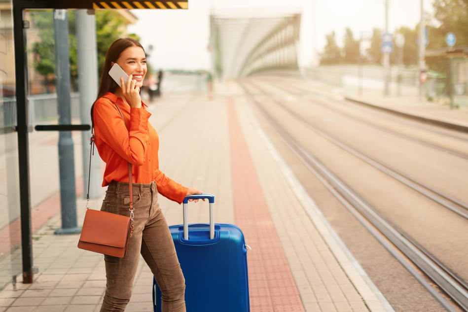 Woman on the phone, wearing an orange shirt, waiting for tram
