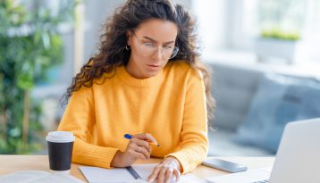 Comptabilité et réduction de TVA - Jeune femme avec un pull orange faisant des comptes