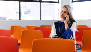 Caucasian woman alone in a conference room using her phone, orange chairs