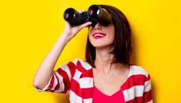 Young woman with binocular, yellow backgroung