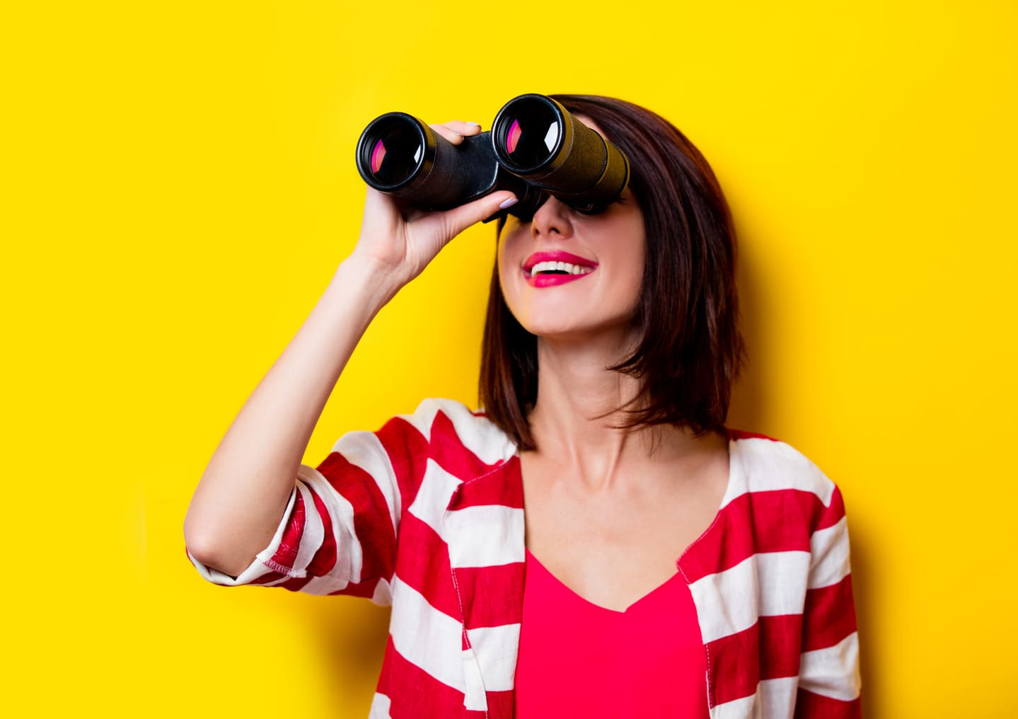 Young woman with binocular, yellow backgroung