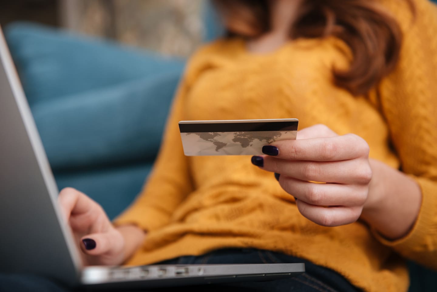 Gros plan d'une femme tenant une carte bancaire dans la main, ordinateur en fond, verso de la carte bancaire avec piste magnétique