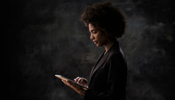 Businesswoman using digital tablet, wearing a black dress, black wall on the brackground