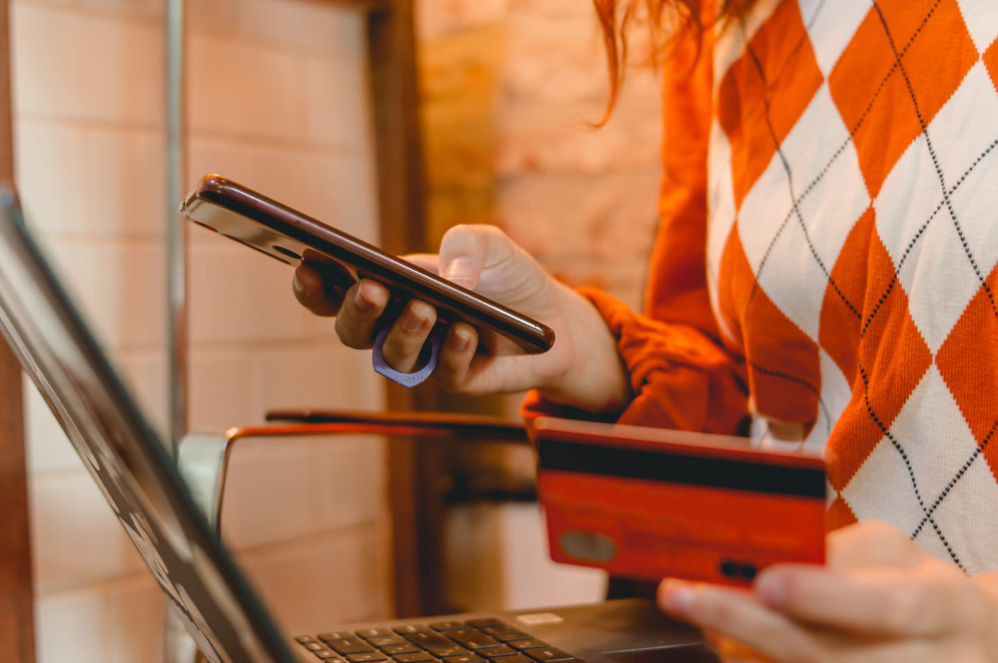 Woman with an orange sweater, looking at her phone and holding a credit card