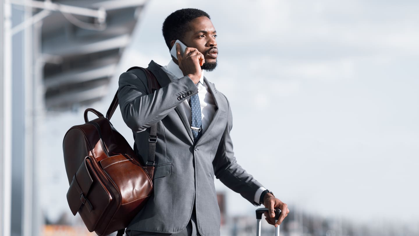 Business man waiting outside of an airport, with a backpack, talking on the phone