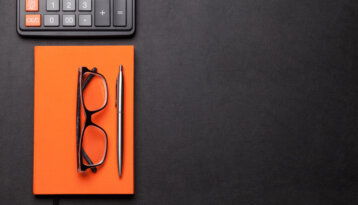 Illustration picture of a calculator, an orange notebook and glasses