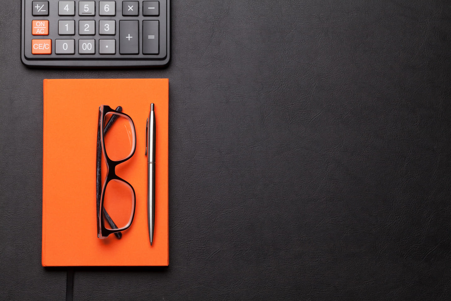 Illustration picture of a calculator, an orange notebook and glasses