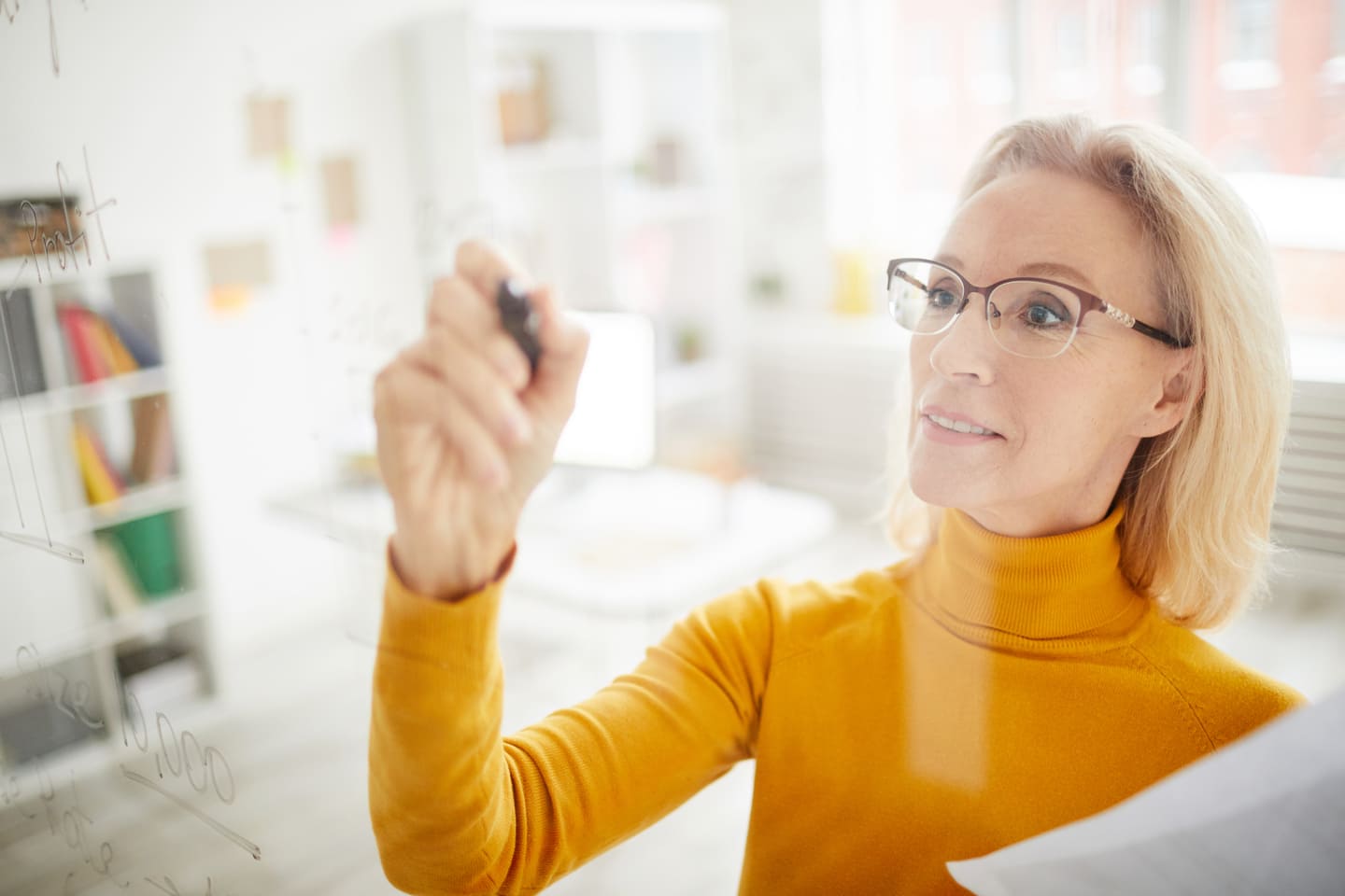 Businesswoman in her 50s writing on glass, with an orange turtleneck